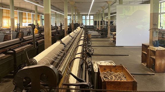 In einer weitläufigen Fabrikhalle stehen zahlreiche aufgereihte historische Textilmaschinen.