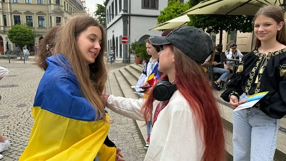 Ein Mädchen mit einer Ukraine-Flagge um den Schultern spricht mit ihrer Freundin