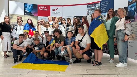 Eine Gruppe von Jungen und Mädchen mit einer auf den Boden gelegten Ukraine-Flagge