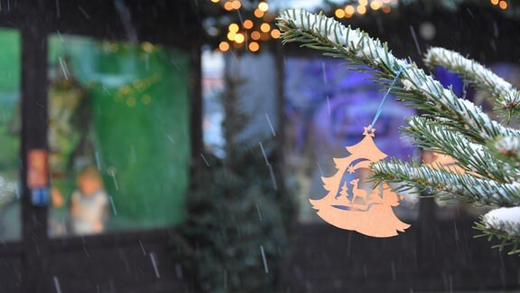 An einem verscheiten Tannenzweig hängt ein weihnachtlicher Anhänger aus Holz mit Baum Reh und Stern.