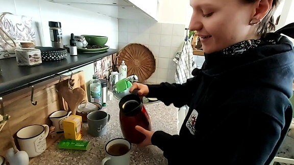 Eine junge Frau steht in einer Küche und gießt sich einen Tee auf.