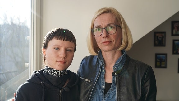 Eine junge Frau mit kurzen braunen Haaren steht neben einer Frau Mitte 40. Beide sehen vertraut aus und blicken in die Kamera. Es ist Jule Pacholke (links) mit ihrer Mutter Simone Födisch. 