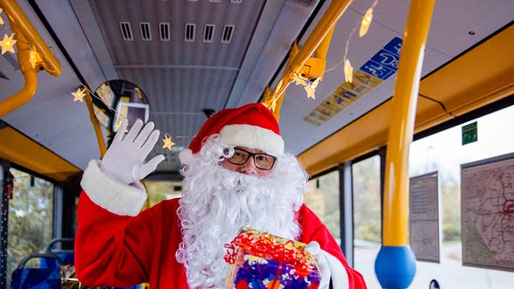 Ein Weihnachtsmannsteht mit einem Geschenk in einem Bus.
