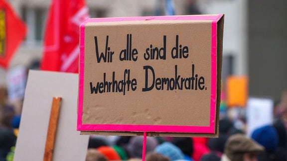 Ein Plakat „Wir alle sind die wehrhafte Demokratie“ wird auf einer Kundgebung gegen Rechtsextremismus am Rathaus gezeigt. 
