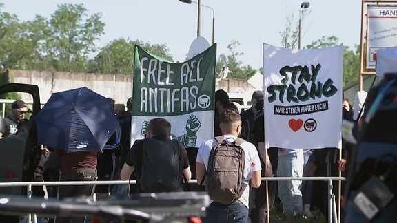 Mehrere Menschen mit Plakaten. Darauf steht teils in englischer Sprache: "Bleib stark. Wir stehen hinter Dir." und "Freiheit allen Antifaschisten"