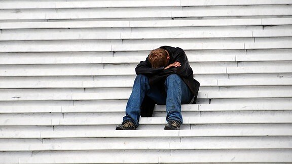Ein Mann sitzt deprimiert auf einer Treppe.