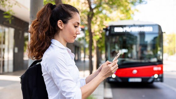 Eine Frau mit einem Handy steht vor einem Bus.