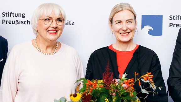 Marion Ackermann, mit einem Blumenstraß und Claudia Roth in hellem Pullover 