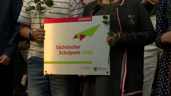 Close-Up von einer kleinen Tafel, gehalten auf einer Bühne: "Gwinner - Sächsischer Schulpreos 2024".