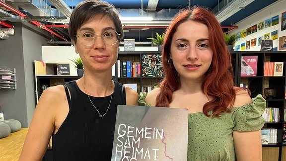 Zwei junge Frauen zeigen ein Buch in die Kamera
