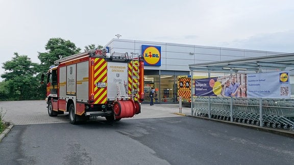 Ein Feuerwehrauto steht vor einem Supermarkt. 