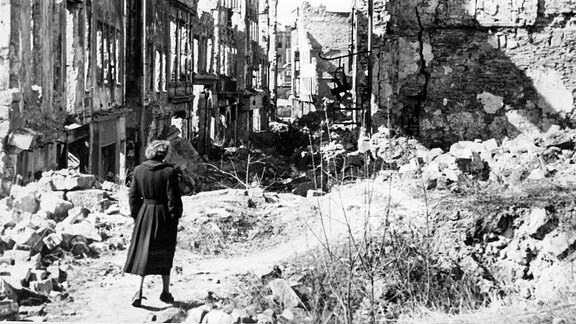 Eine Frau geht in einer Straße in Dresden an Häusern vorbei, von denen nach dem Zweiten Weltkrieg nur noch Ruinen geblieben sind