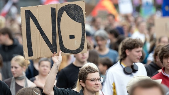 Teilnehmer einer Demonstration gegen Rechtsextremismus und für Demokratie gehen über den Theaterplatz und halten ein Schild mit der Aufschrift „NO“.