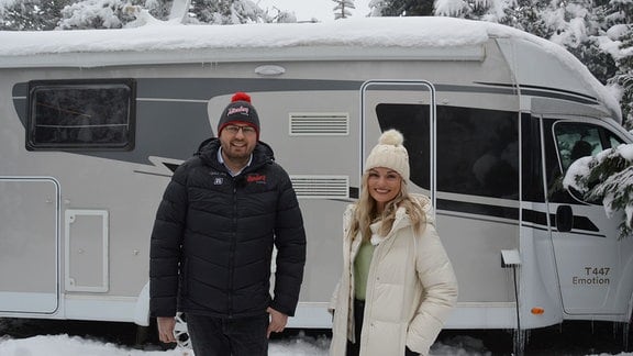 Ein Mann und eine Frau stehen vor einem winterlich zugeschneiten Wohnmobil.