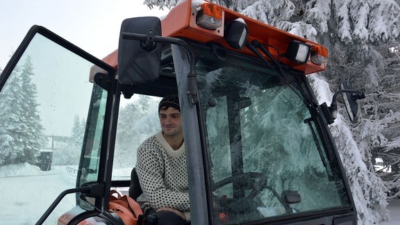 Ein junger Mann sitzt im Führerhaus eines Schnee-Räumgerätes.