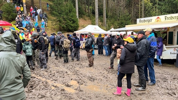 Menschen stehen bei einer Veranstaltung mitten im Wald im Matsch.