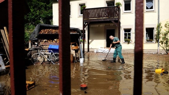 Ein Mann versucht am 16.08.10 in Bad Schandau in der Saechsischen Schweiz vor einem Haus an der ueberfluteten Kirnitzschtalstrasse das Hochwasser wegzukehren.