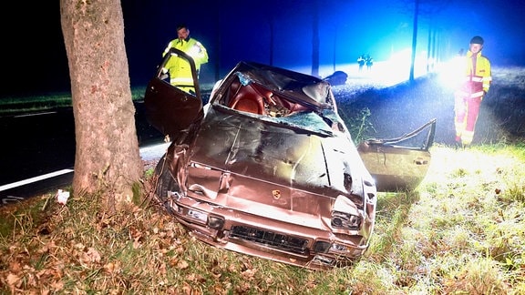 Ein Auto mit Totalschaden steht an der Straße, im Hintergrund liegt der Körper des Pferdes.