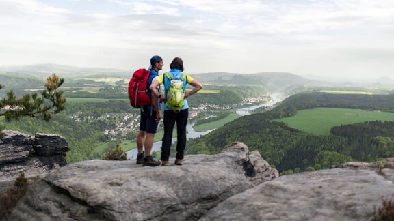 Wanderer stehen an einem Aussichtspunkt auf dem Berg Lilienstein und betrachten die Elbe und den Nationalpark Sächsische Schweiz.