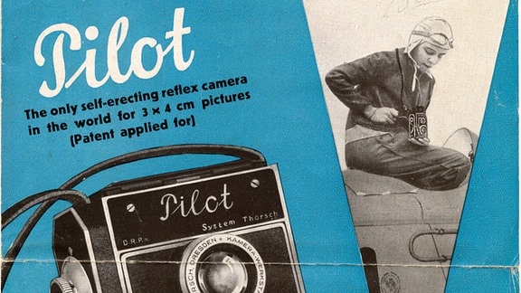 Werbeplakat aus den 1930er-Jahren in blau, schwarz und weiß, auf dem eine Kamera zu sehen ist; im Anschnitt ist ein Pilot zu sehen, der die Kamera benutzt