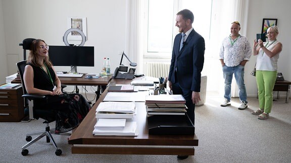 Michael Kretschmer (CDU, M), Ministerpräsident von Sachsen, steht zum Tag des offenen Regierungsviertels in seinem Büro in der Staatskanzlei vor Emily Schön (l), Besucherin, die an seinem Schreibtisch sitzt. 
