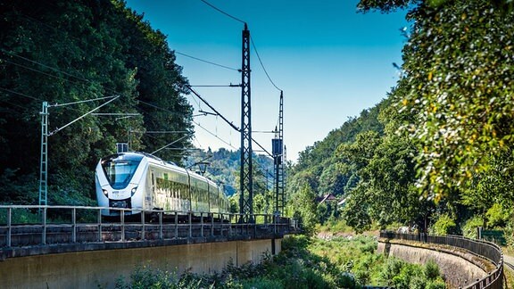 Eine Regionalbahn fährt in den Sommerferien 2020 richtung Dresden. Man sieht einen Zug der Mitteldeutschen Regionalbahn (MRB) an einem Flusslauf vorbeifahren. 