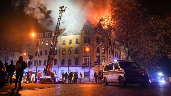 Dachstuhl eine Mehrfamilienhauses brennt, Feuerwehrmänner löschen von einer Fahrzeugleiter aus die Flammen