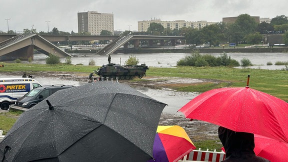 Menschen mit Regenschirmen vor eingestürzter Carolabrücke.