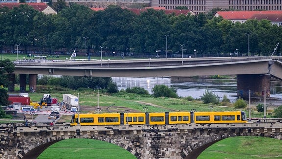 Blick auf den vom Einsturz bedrohten Teil der Carolabrücke während im Vordergrund eine Straßenbahn der Dresdner Verkehrsbetriebe (DVB) über die Augustusbrücke fährt.