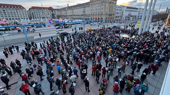 Menschen stehen vor einer improvisierten Bühne in Dresden und singen gemeinsam.