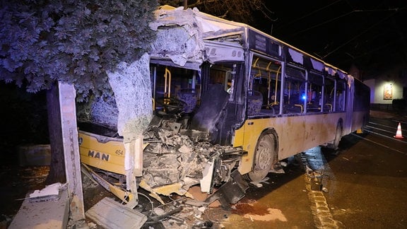 Ein gelber Gelenkbus ist nach einem Unfall schwer beschädigt, die Front eingedrückt und aufgerissen. 