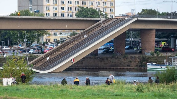 Menschen stehen am Elbufer und schauen auf die eingestürzte Brücke.