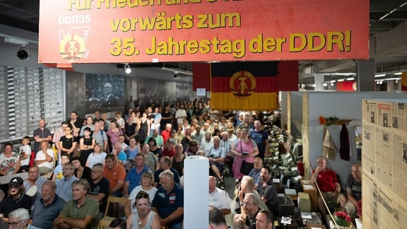 Teilnehmer stehen und sitzen während einer Versteigerung in den Ausstellungsräumen des bereits geschlossenen Museums Welt der DDR
