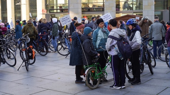 Zwei Frauen stehen mit drei Kindern in einer Gruppe. Sie halten zwei Fahrräder. Im Hintergrund tummeln sich viele weitere Menschen mit Fahrrädern.