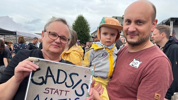 Eine Frau hält ein Demonstrationsposter in die Kamera. Neben ihr steht ein Mann, der ein Kleinkind trägt.