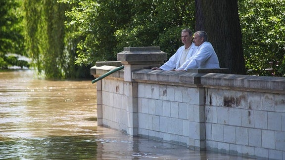 Zwei Männer stehen an einem Fluss der Hochwasser führt.
