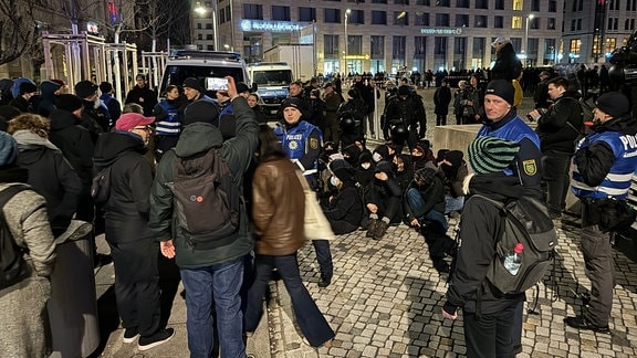 Junge Menschen sitzen auf einer Straße und blockieren den Zugang zum Altmarkt in Dresden am 13.2.2024 für Neonazis, Rechtsradikale und AfD-Anhänger.