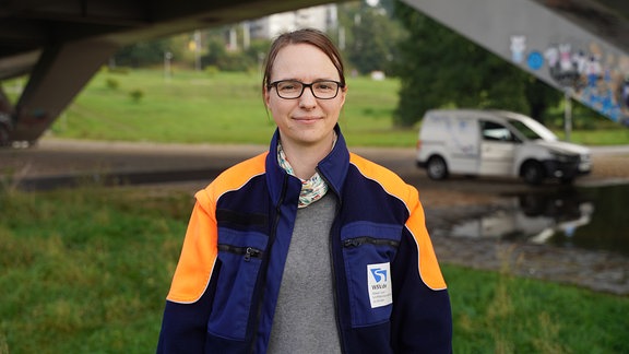 Eine Frau mit Brille schaut freundlich in die Kamera. Sie trägt eine blau-orange Regenjacke.