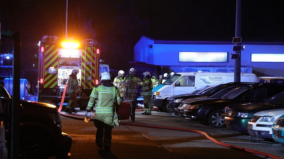 Feuerwehrleute sammeln sich bei einem nächtlichen Einsatz auf einem Parkplatz.