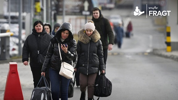 Personen, in dicken Jacken gekleidet, laufen mit Reisetaschen auf einer Straße. 