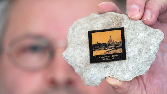 Torsten Daae, Geschäftsführer, hält einen Stein des abgerissenen Brückenteils C der eingestürzten Carolabrücke mit einer Plakette in seinem Laden „Catapult“.