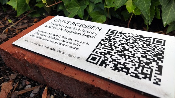 Ein Pflasterstein auf einer Grabwiese, auf dem sich ein QR-Code befindet. 