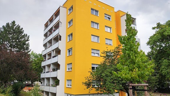 Ein Wohnblock mit gelber Häuserwand umringt von Bäumen und Wiese.