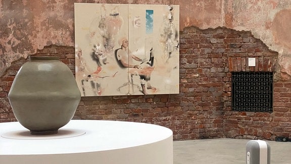  eine Vase steht auf einem runden Podest, dahinter hängt ein abstraktes Gemälde an der Wand. 