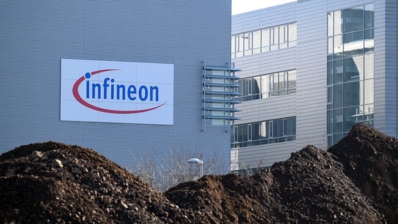 Firmengebäude von Infineon sind hinter einem Erdhaufen auf der Fläche für ein neues Werk zu sehen. 