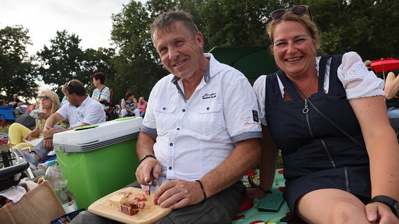 Ein Pärchen sitzt beim Abendpicknick auf den Elbwiesen und feiert auf den Elbwiesen Schlagerstar Roland Kaiser, der nebenan auf dem Konzertgelände singt.