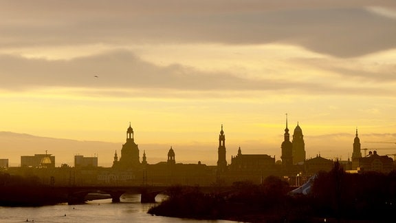 Die Kulisse der Altstadt mit der Frauenkirche (l-r), dem Ständehaus, der Katholischen Hofkirche, dem Hausmannsturm, dem Rathausturm und der Kreuzkirche zeichnen sich bei Sonnenaufgang als Silhouette ab.