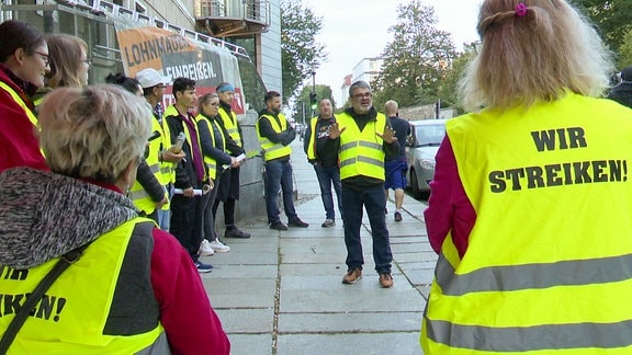 Mehrere Menschen streiken vor einem Gebäude. 