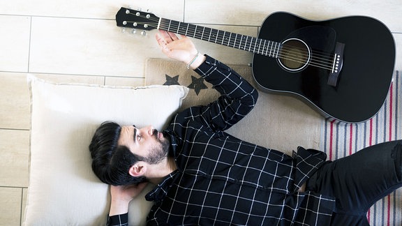 Junger Mann liegt zu Hause auf dem Boden neben der Gitarre.