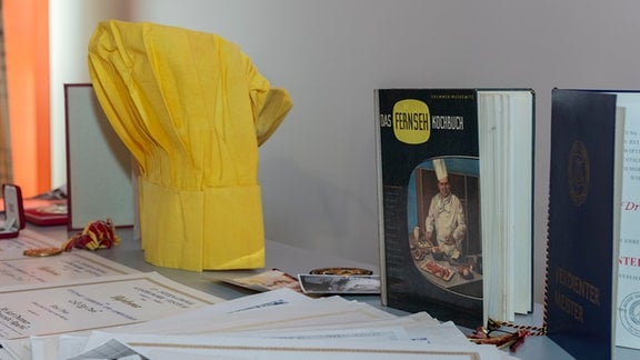 Eine gelbe Kochmütze neben dem Buch "Das Fernseh Kochbuch".